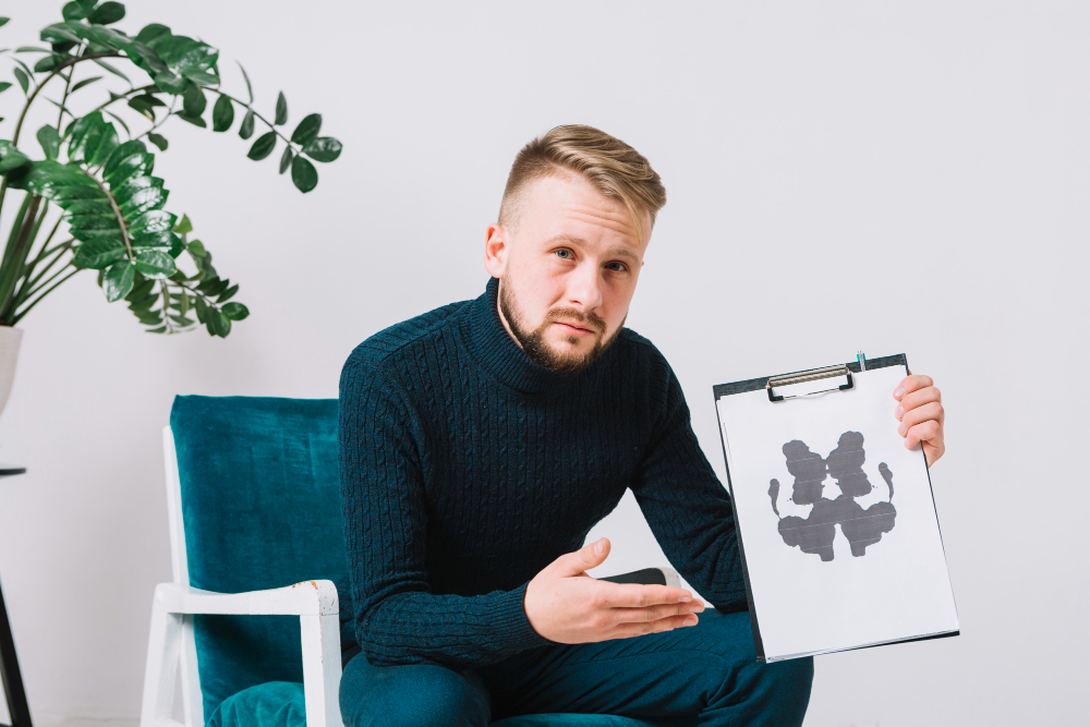 confident-young-male-psychologist-sitting-arm-chair-showing-rorschach-inkblot-test-paper