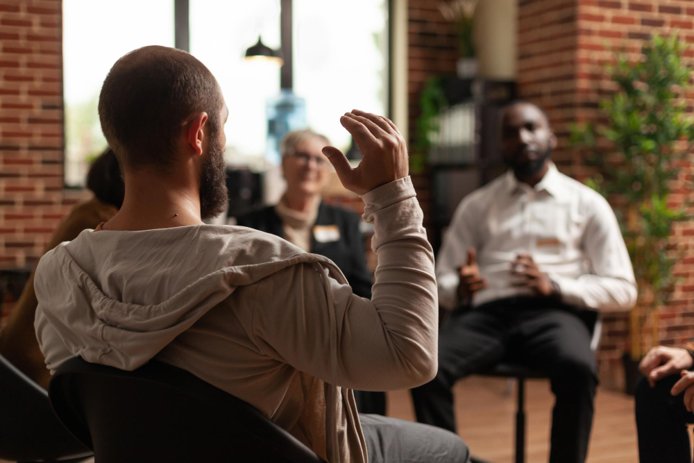 man-with-addiction-sharing-mental-health-issues-with-group-aa-meeting-talking-therapist-people-having-conversation-about-depression-rehabilitation-therapy-session